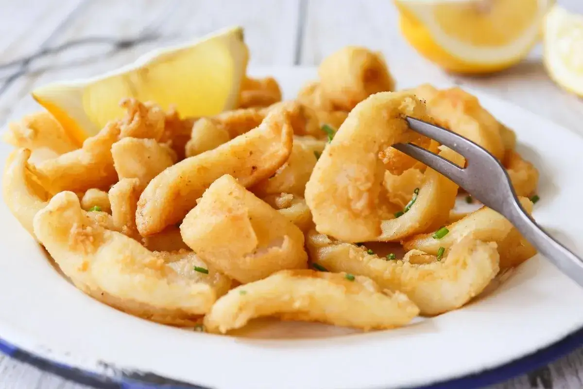 Un plato de chocos fritos crujientes, adornado con gajos de lim&oacute;n y perejil picado. Un tenedor se alza listo para probar esta delicia.