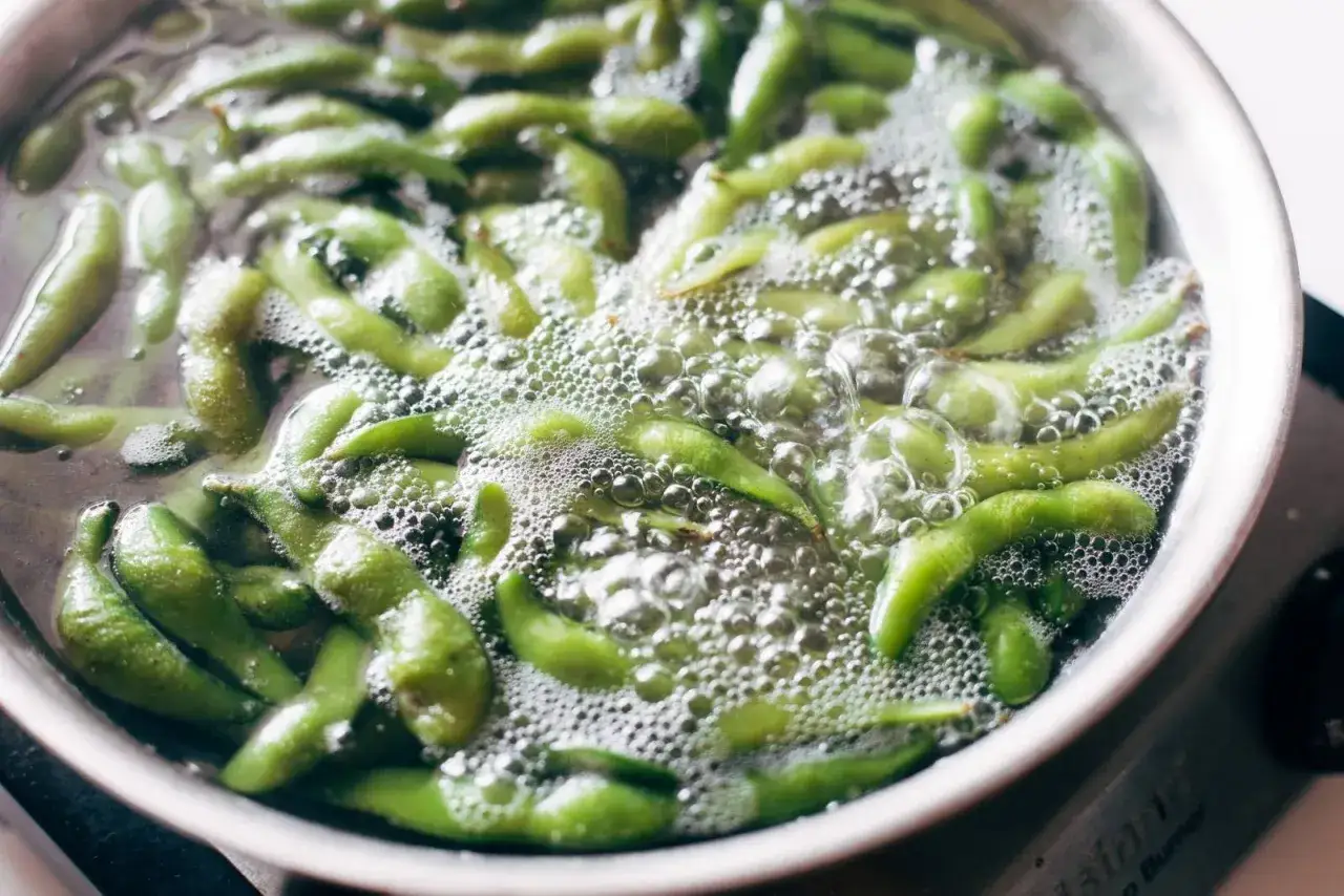 Gr&uuml;ne Edamame-Schoten kochen in sprudelndem Wasser. Was ist Edamame? Junge Sojabohnen, eine gesunde Snack-Option.