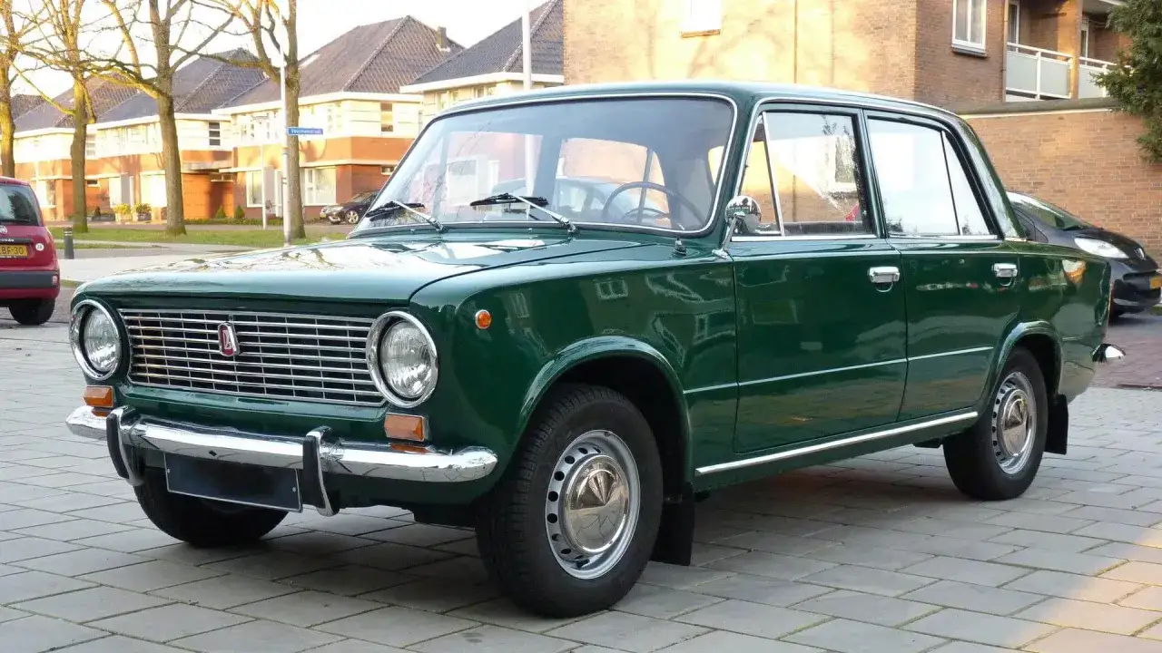 Grüner Lada Oldtimer parkt auf gepflastertem Weg vor Häusern.