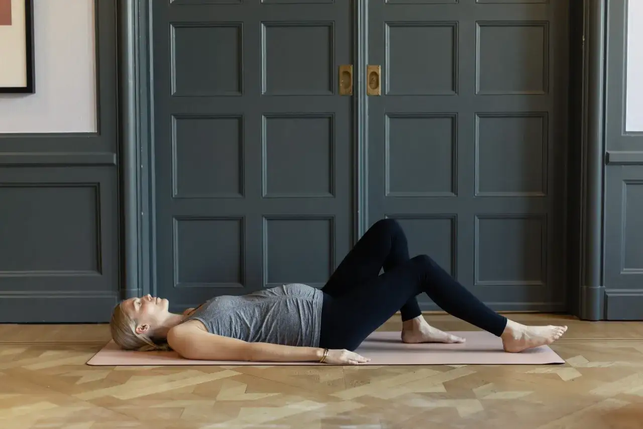 Gravid kvinna med ont i ryggen ligger p&aring; en yogamatta och g&ouml;r en &ouml;vning f&ouml;r att lindra sm&auml;rtan.