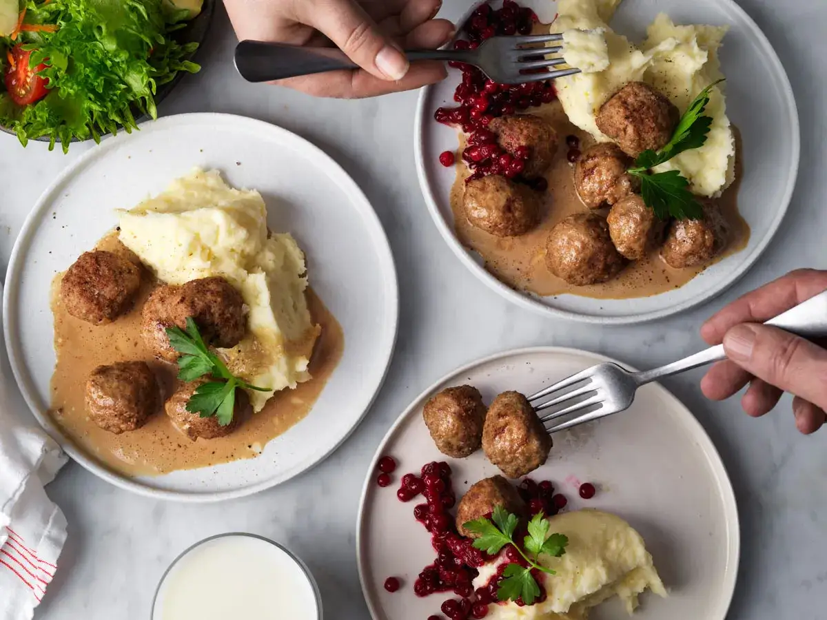 Tre tallrikar med köttbullar, potatismos och gräddsås. Lingon och persilja som garnering. Ett perfekt minutfile recept för en mysig middag.