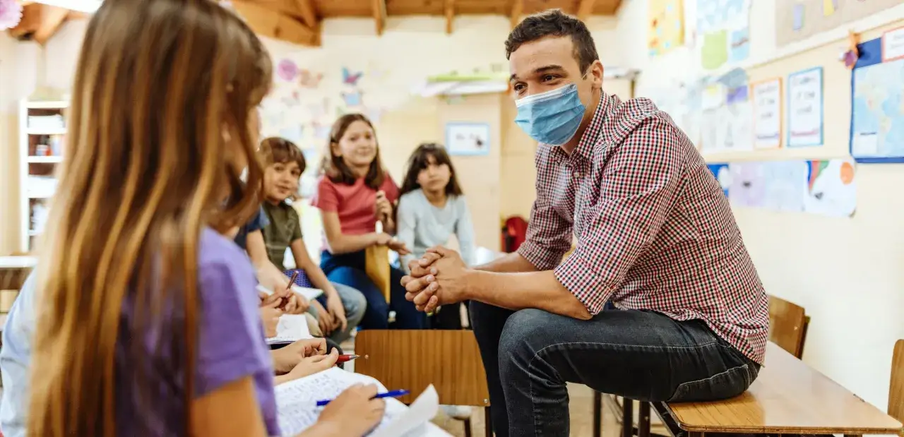 Un insegnante con mascherina blu ascolta gli alunni in classe. Il **bes significato** &egrave; l'inclusione di tutti, anche in tempi difficili.