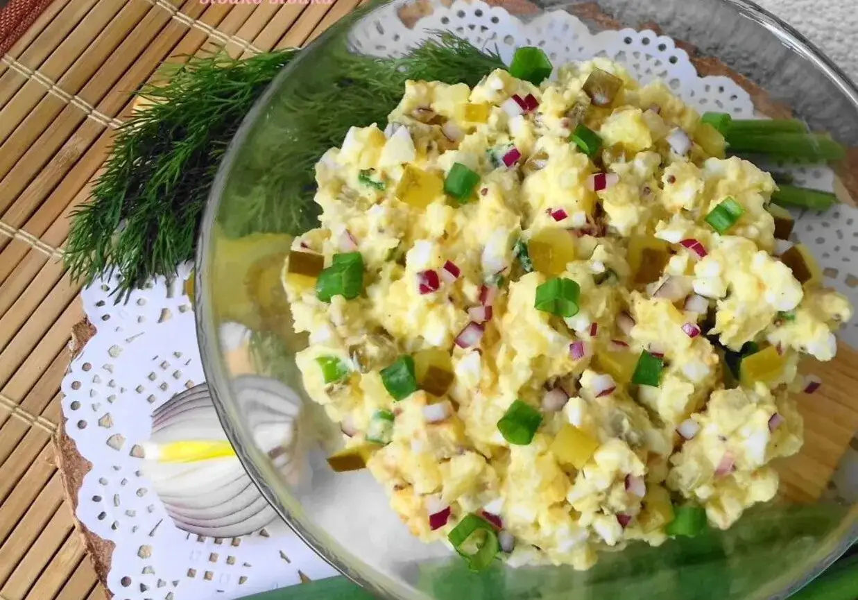 Pyszny kartofel salad z jajkiem, ogórkiem kiszonym i szczypiorkiem, podany w szklanej misce.