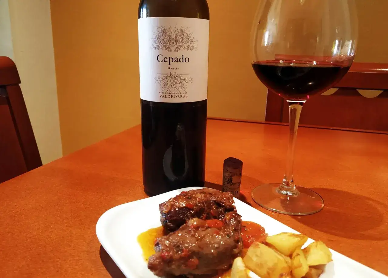 Delicioso plato de carrilleras estofadas con patatas, acompañado de una copa de vino tinto Cepado Mencía, perfecto vino para carrilleras.