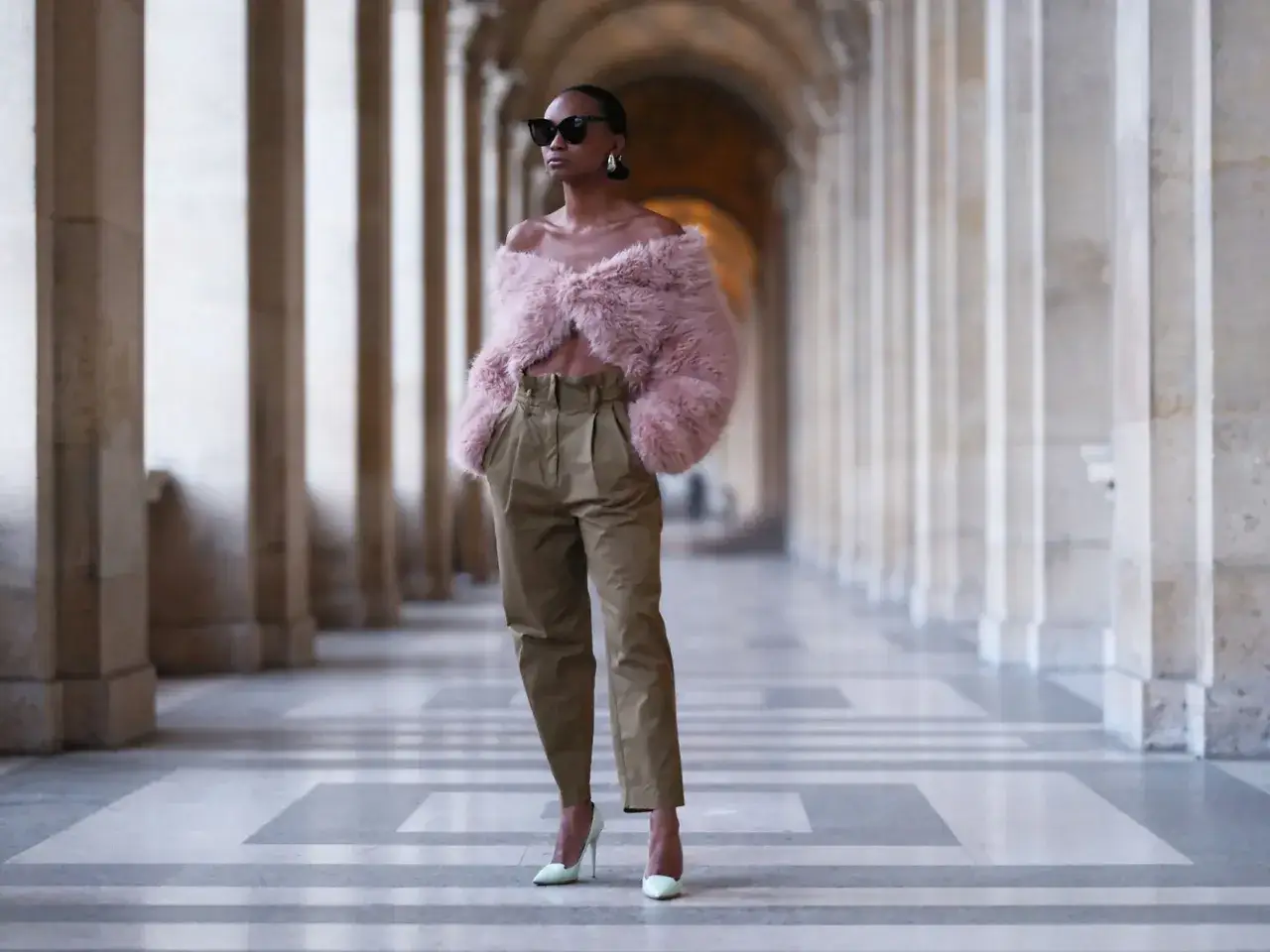 Eleganckie spodnie z wysokim stanem i puchaty r&oacute;żowy top tworzą modną stylizację. Kobieta w okularach przeciwsłonecznych prezentuje outfit na tle arkad.
