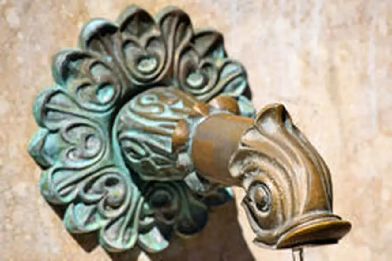 Robinet ancien en bronze orné, patine vert de gris, avec un bec en forme de poisson stylisé.