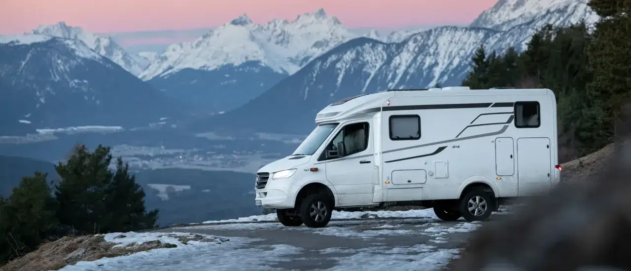 Husbil parkerad på en bergsväg med snöklädda berg i bakgrunden. Perfekt för året runt camping.