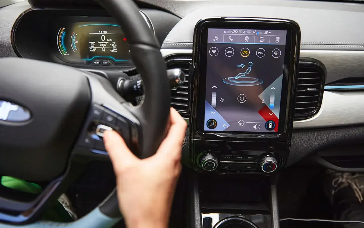 Interno auto con cruscotto digitale e schermo touch. La mano del conducente interagisce con i comandi. Il sistema dr 1.0 &egrave; attivo.