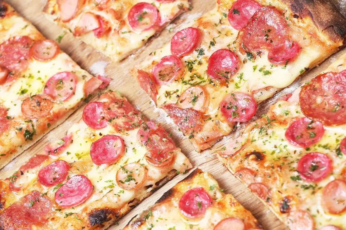 Kawałki pizzy z kiełbasą i serem, posypane ziołami. Idealne ciasto na pizzę dla każdego smakosza.