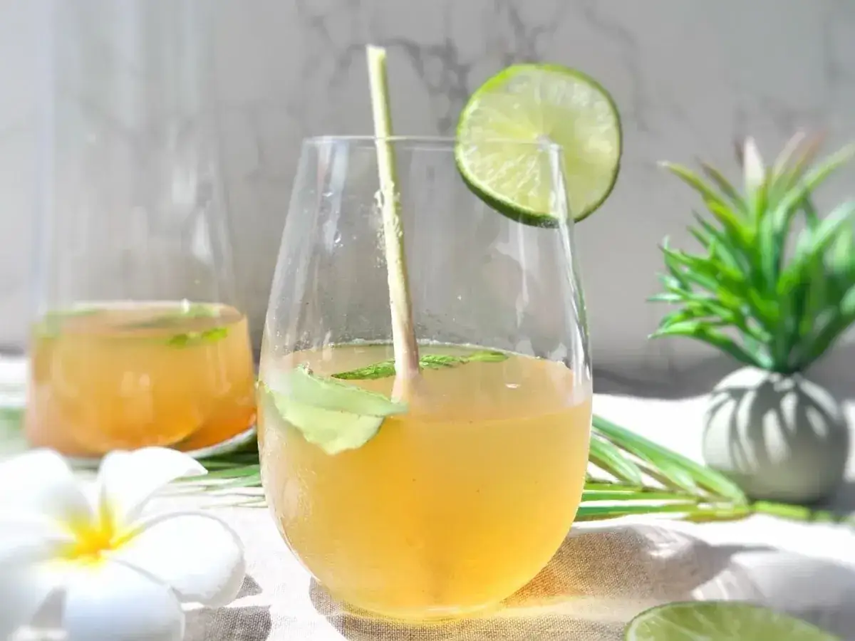 Verre rempli d'une infusion gingembre citron rafraîchissante, garni d'une tranche de citron vert et de menthe.