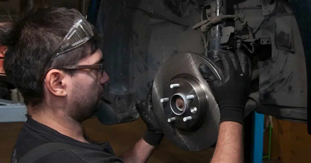 Mechanik w okularach ochronnych dokonuje wymiany klocków hamulcowych, trzymając nowy, lśniący tarczę hamulcową.
