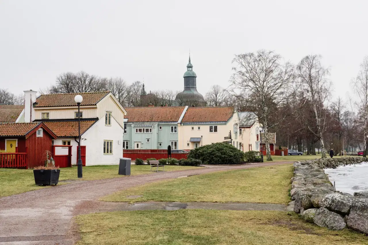 Färgglada hus i Vadstena, med en kyrka i bakgrunden. En promenadstig leder mot en isbelagd sjö.