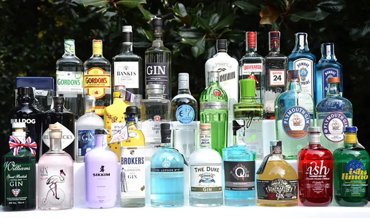Kolekcja butelek z alkoholem, głównie dżin, w różnych kształtach i kolorach, gotowa na przyjęcie.