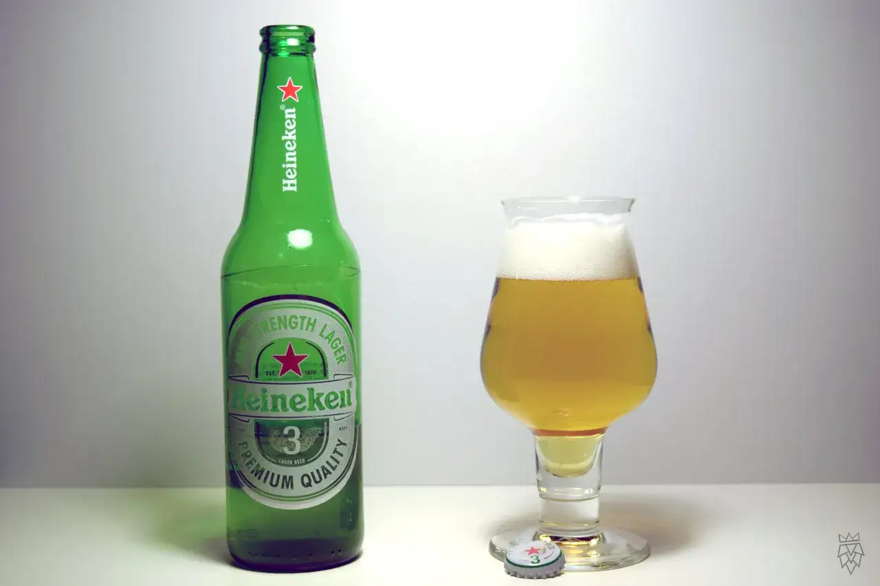 Zielona butelka piwa Heineken obok szklanki z orzeźwiającym lagerem. Idealny duet na letnie popołudnie.
