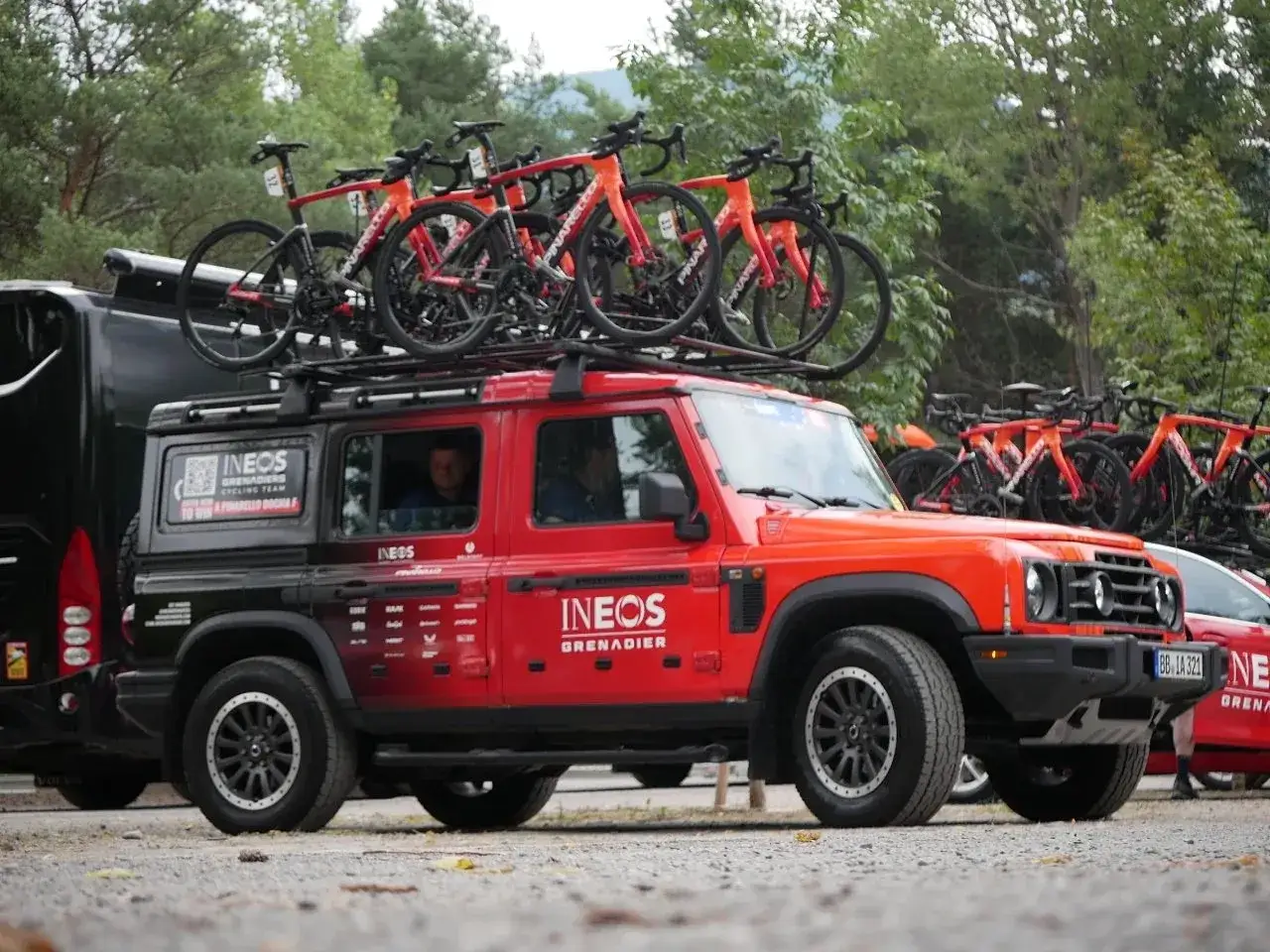 Rotes Fahrzeug des Teams INEOS Grenadiers mit Rennrädern auf dem Dach.