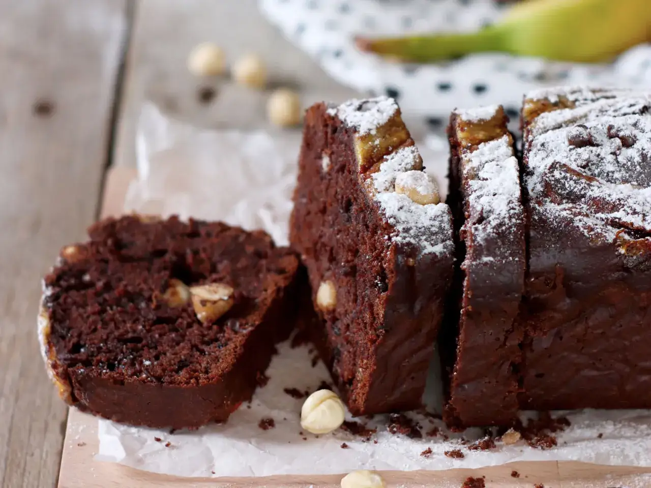 Fetta di torta al cioccolato e banana, cosparsa di zucchero a velo e nocciole. Un dolce che ricorda il gelato alla banana.