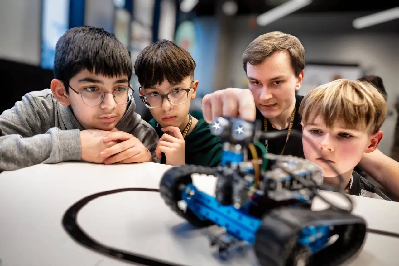 Junge Schüler und ein Lehrer bauen und untersuchen einen Roboter. Sie sind konzentriert und engagiert, was das Lernen der Zukunft widerspiegelt.