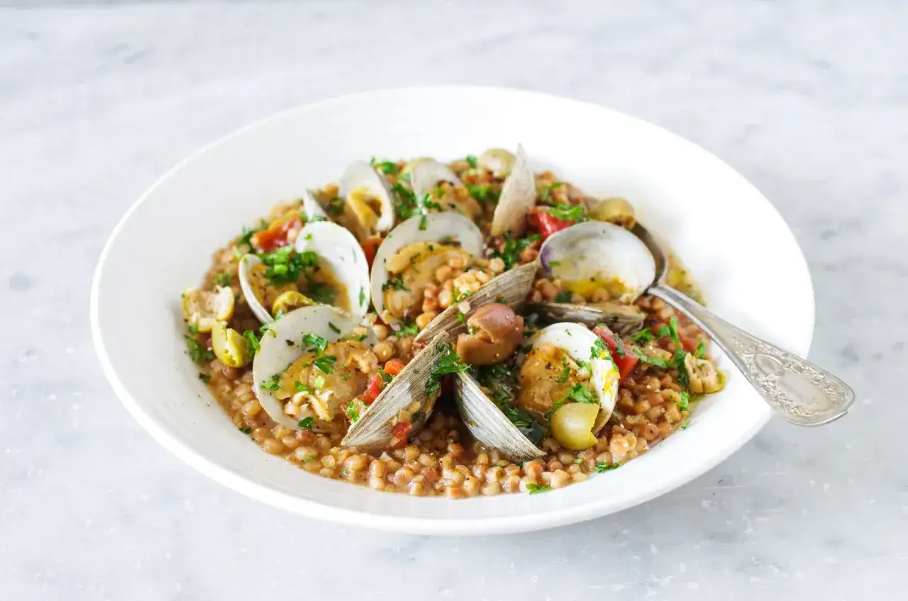 Fregola Sarda Rezept: Herzhafte Pasta mit Muscheln, Oliven und Tomaten, garniert mit frischer Petersilie. Ein Genuss!