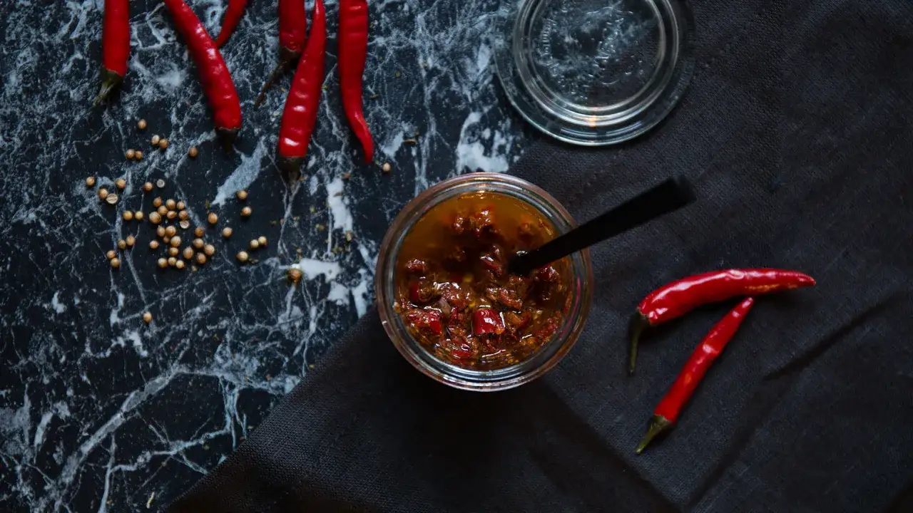 Ein Glas mit selbstgemachter Harissa-Paste, umgeben von frischen Chilischoten und Koriandersamen. Perfekt f&uuml;r jedes Harissa Rezept.