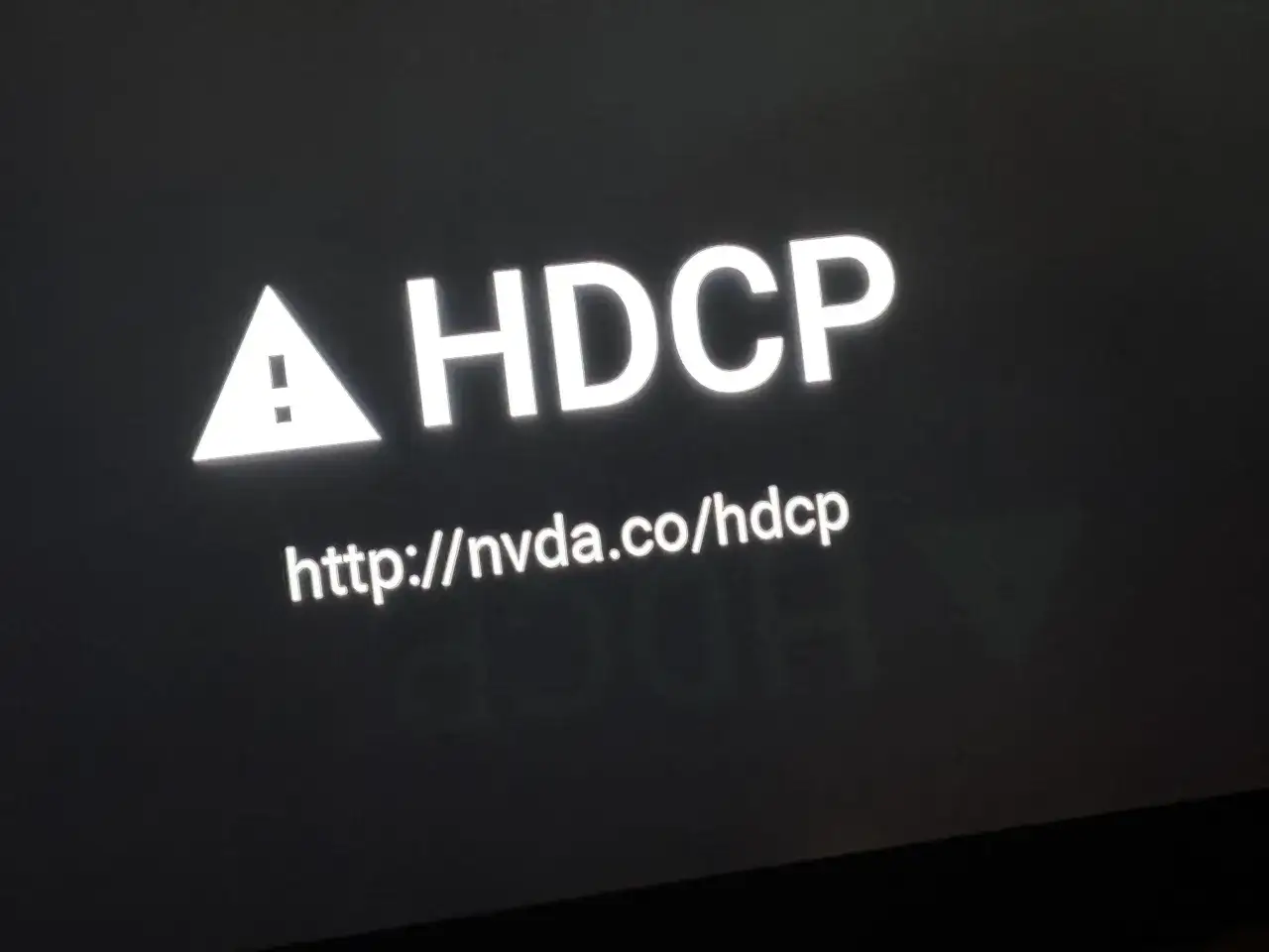 Biały trójkąt z wykrzyknikiem i napis HDCP. Poniżej adres http://nvda.co/hdcp. Dowiedz się, hdcp co to jest.