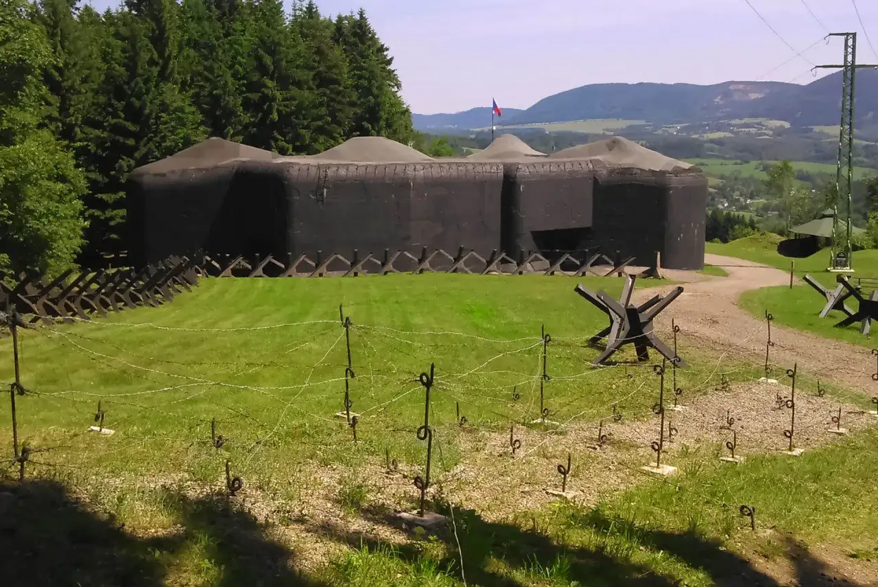 Trutnov atrakcje: bunkry linii obrony z czasów wojny, druty kolczaste i zapory przeciwczołgowe na tle zielonych wzgórz.