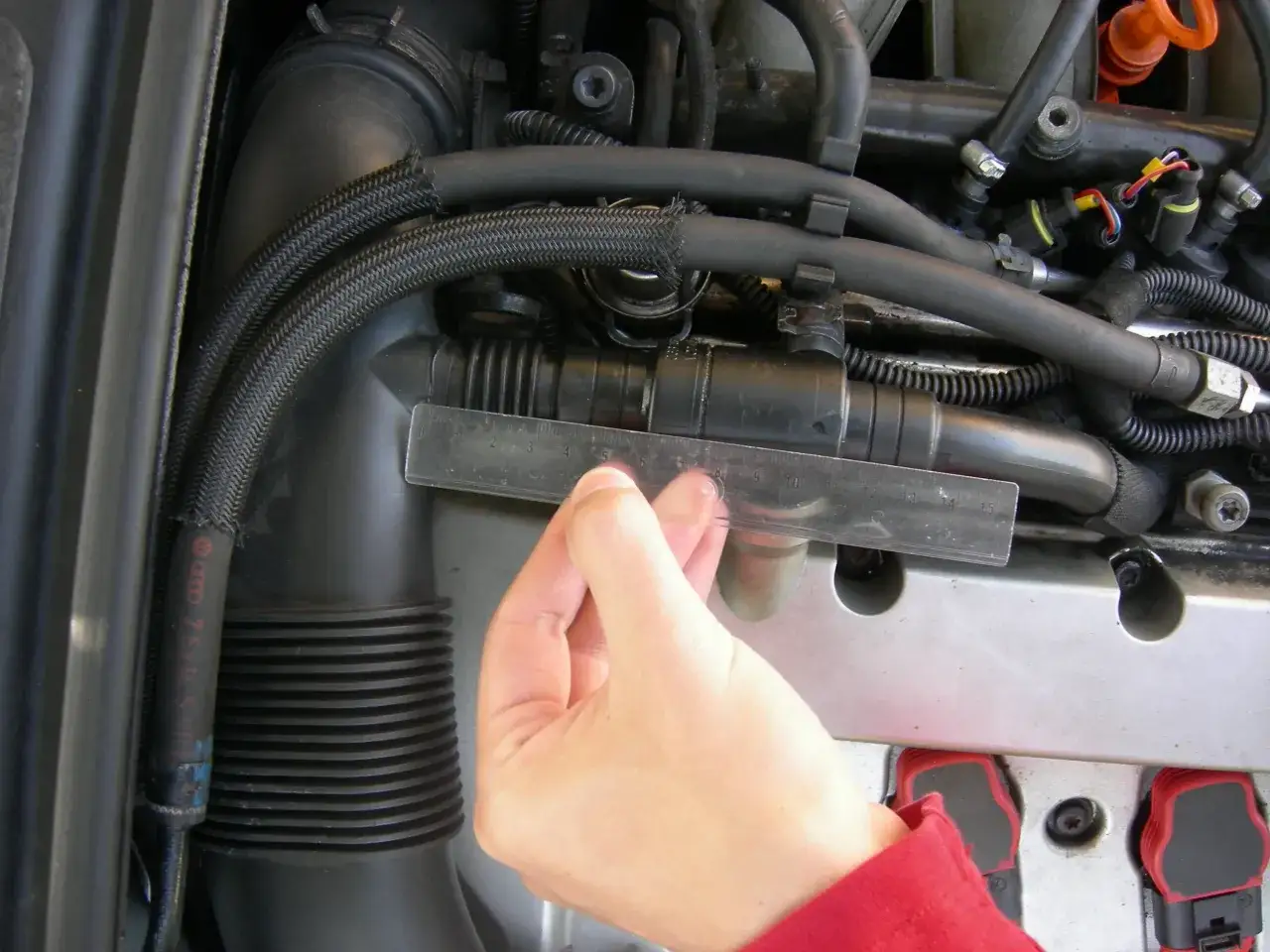 Wymiana odmy Audi A4 B6 2.0: ręka z linijką mierzy średnicę przewodu w silniku.
