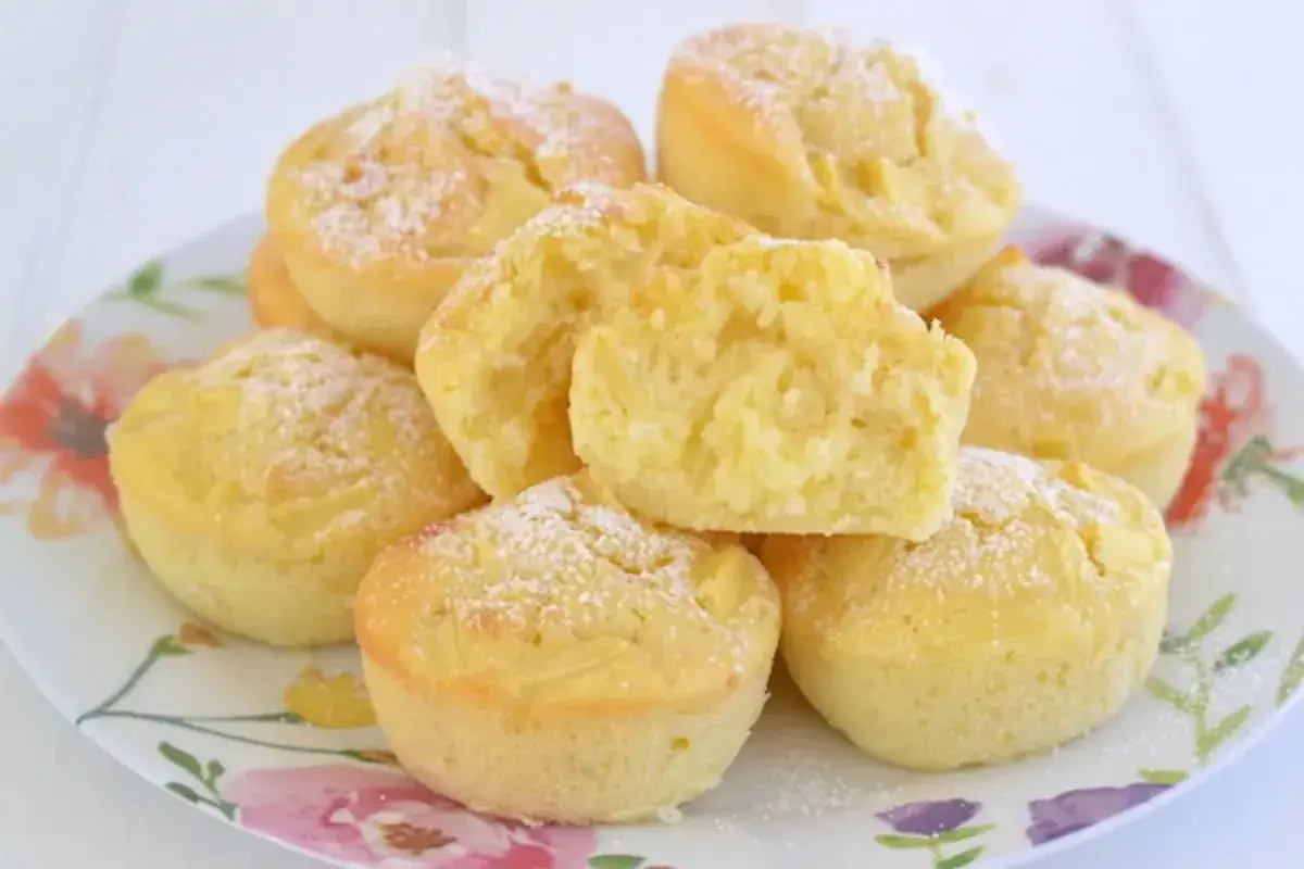 Un piatto di muffin alle mele soffici, spolverati di zucchero a velo. Uno è tagliato a metà, mostrando la morbida mollica e i pezzetti di mela.