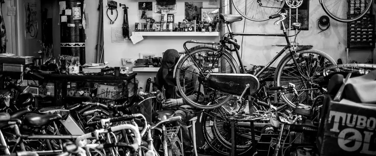 Warsztat rowerowy, gdzie mechanik przygotowuje rower do sezonu. W tle półki z częściami i narzędziami.