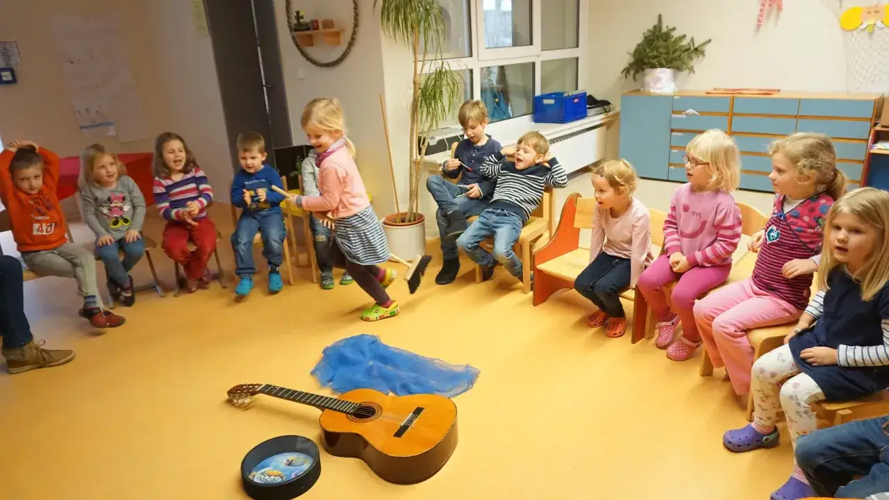 Kinder sitzen im Kreis, ein M&auml;dchen fegt mit einem Besen. Tip tap, die Musik beginnt.