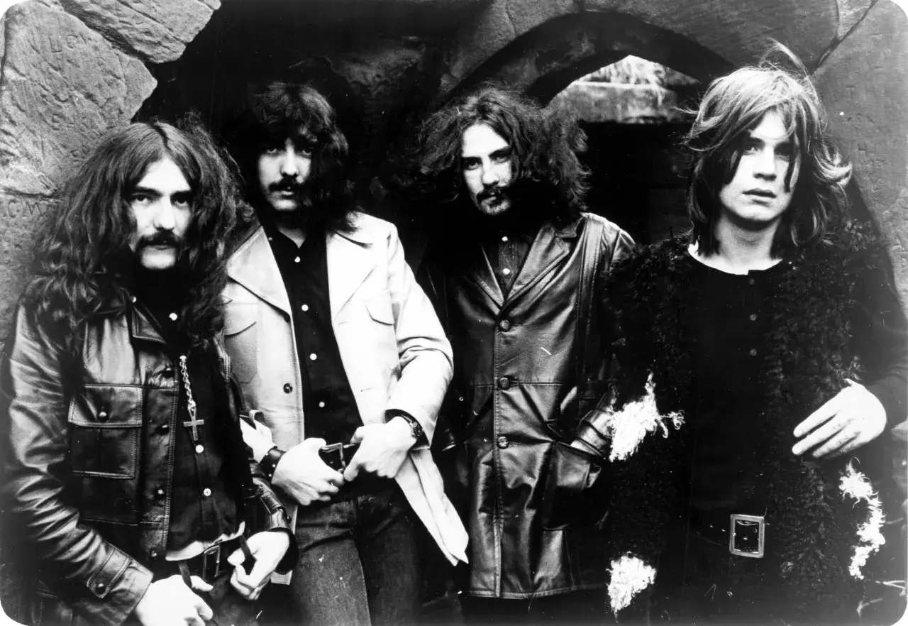 Czterech muzyków Black Sabbath, w tym wokalista, pozuje w mrocznym otoczeniu.