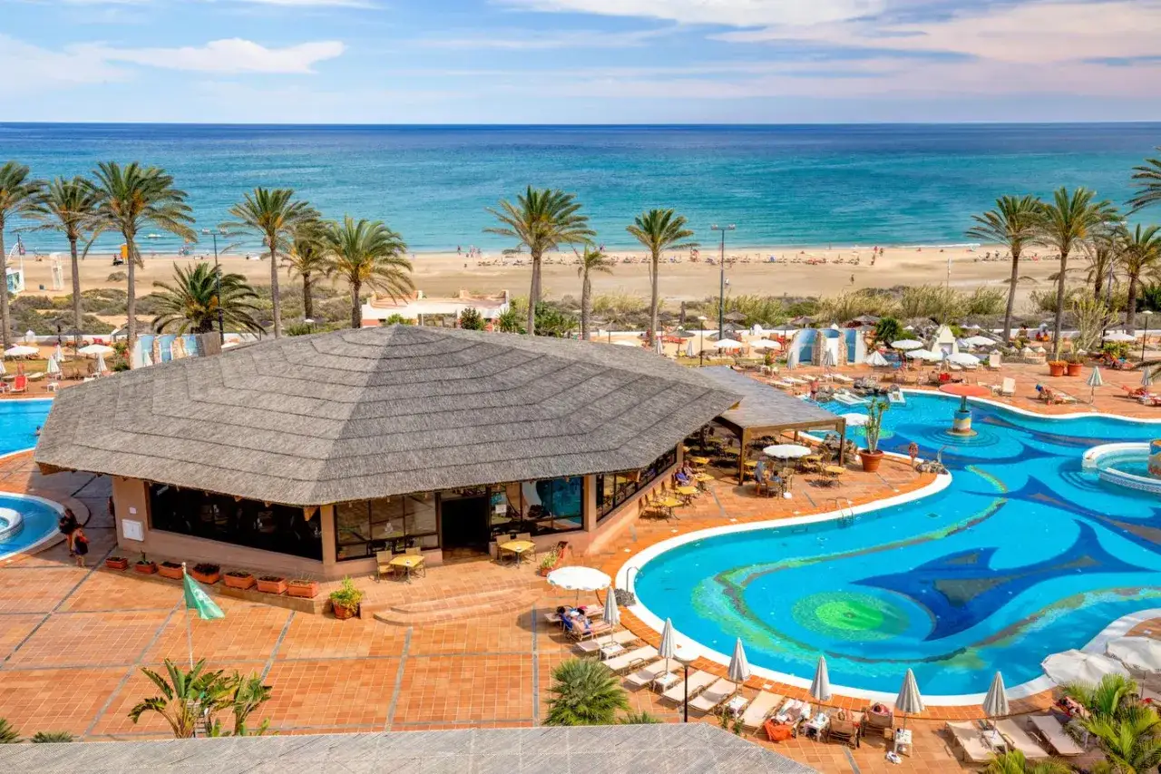 Einladender Poolbereich mit Palmen und Blick auf den Strand und das Meer. Das Costa Calma Palace bietet Entspannung pur.