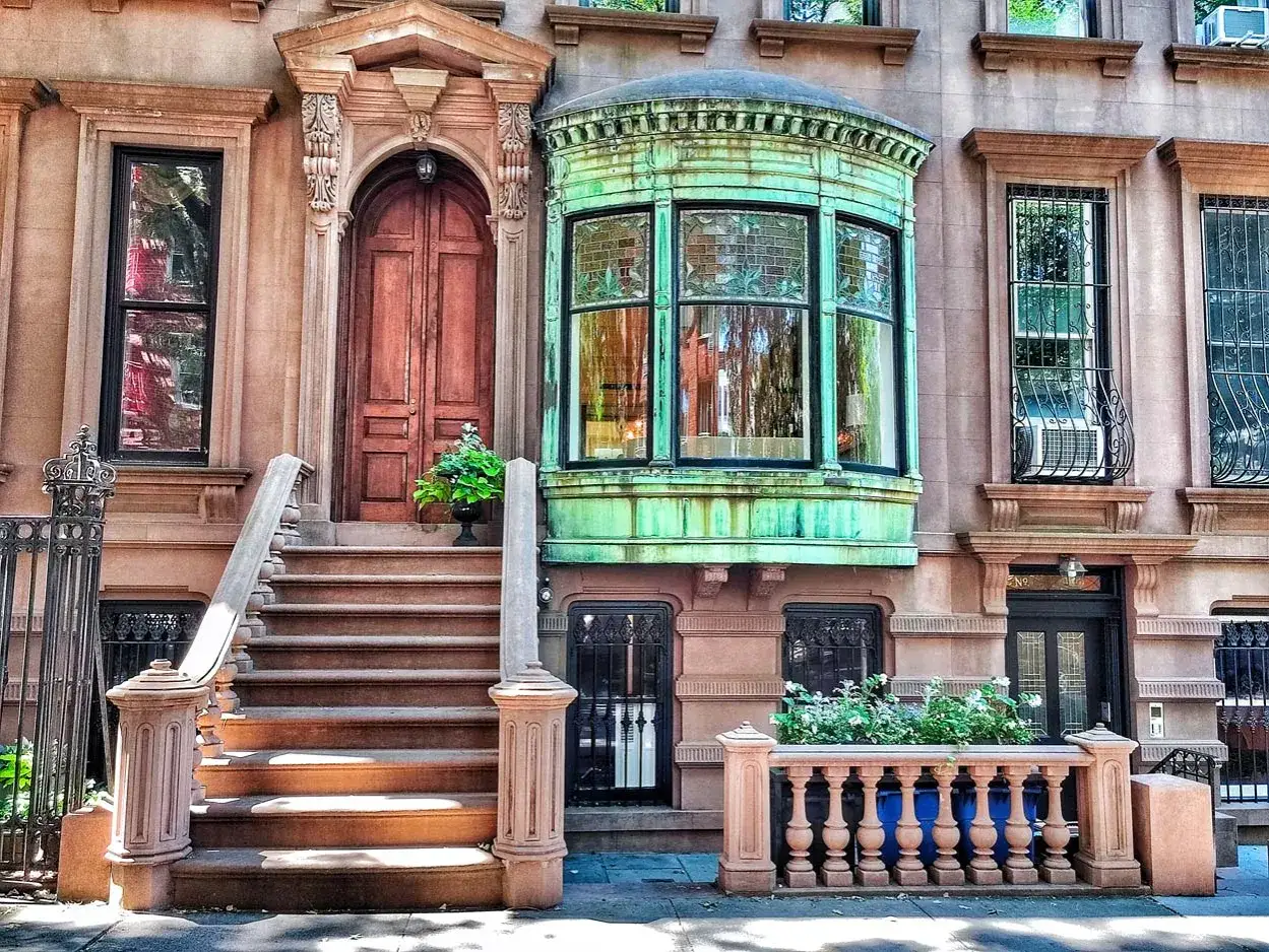 Kamienica w **Brooklyn** z zieloną werandą, drewnianymi drzwiami i schodami prowadzącymi do wejścia.