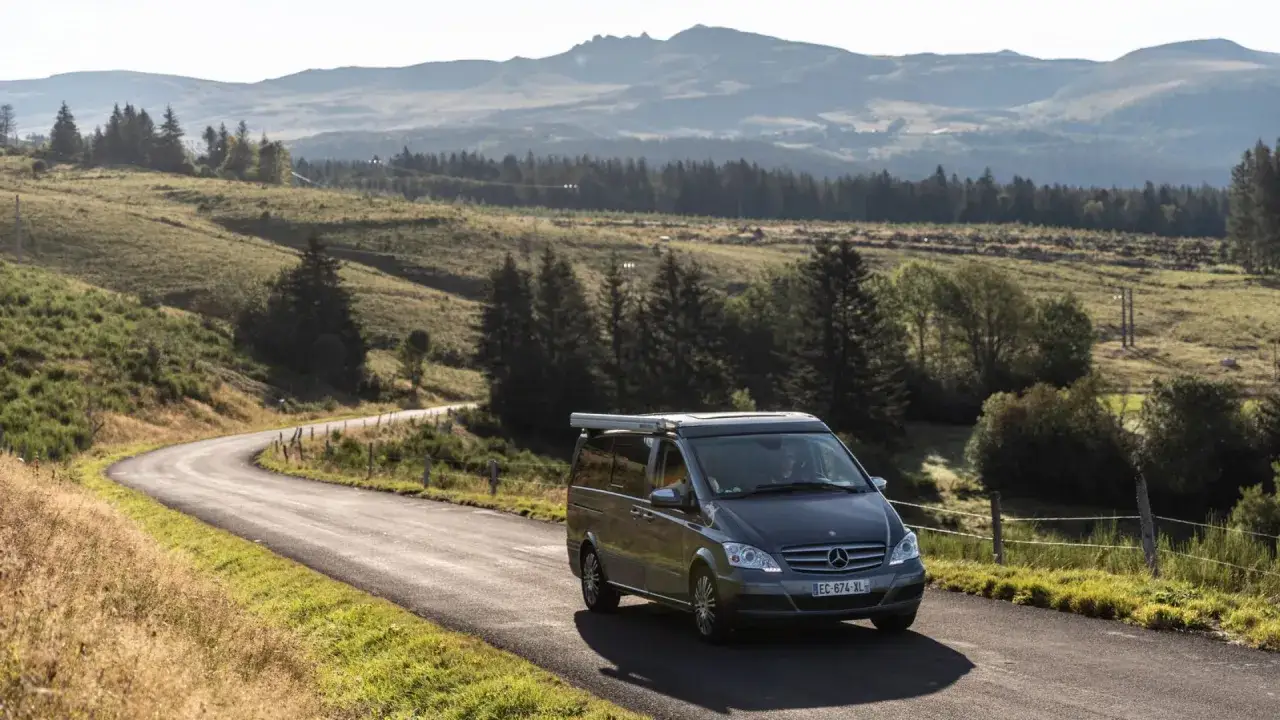 Camping-car Mercedes sur une route sinueuse en Auvergne, paysage vallonné et verdoyant. Une aire de camping-car gratuite vous attend !