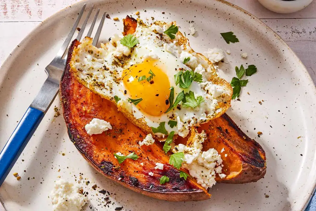Une patate douce rôtie garnie d'un œuf au plat, de fromage émietté et de persil. Un petit-déjeuner savoureux et coloré.