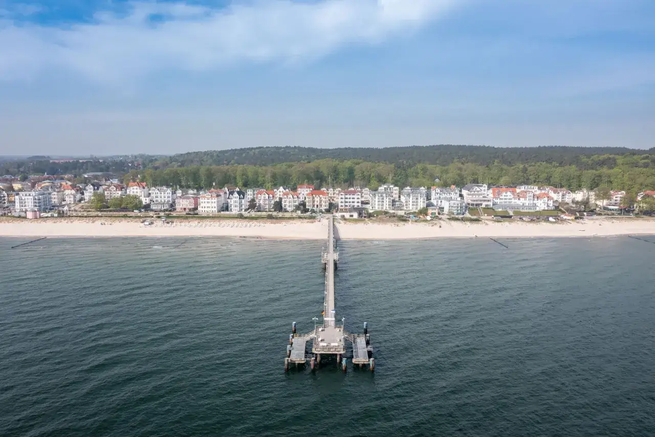 Blick auf den Strand von Bansin mit Seebrücke, weißen Häusern und grünen Wäldern im Hintergrund.