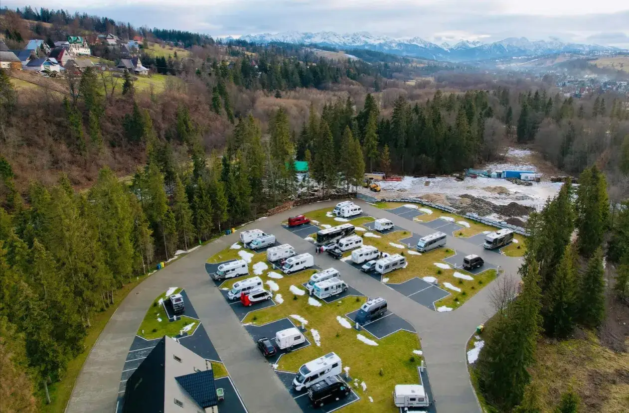 Kampery i przyczepy kempingowe na polu namiotowym w górach. Widok z lotu ptaka na camping ustup z widokiem na ośnieżone szczyty.