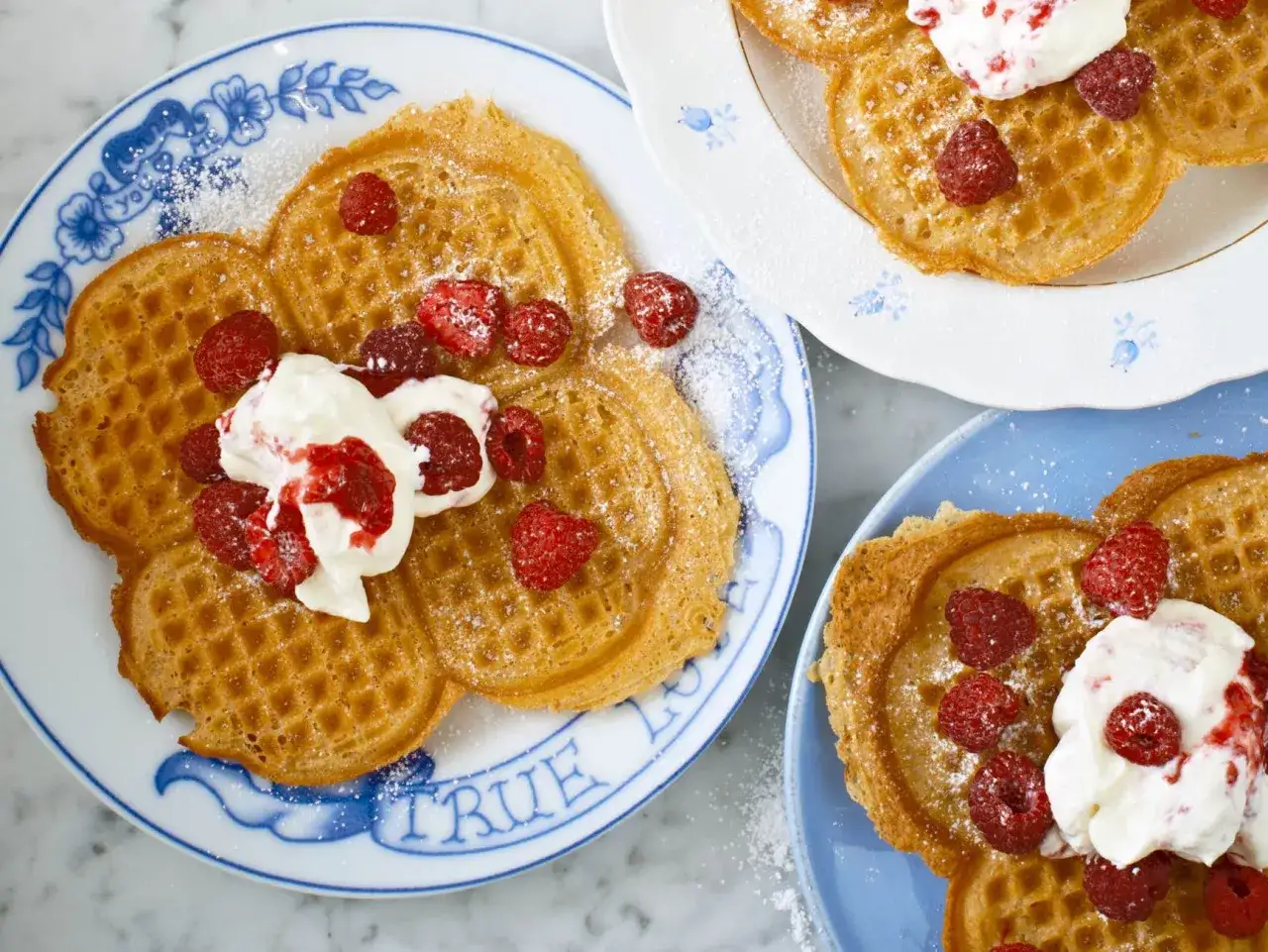 Nyttiga våfflor med hallon och grädde på blåvita tallrikar. En härlig frukost eller fika!