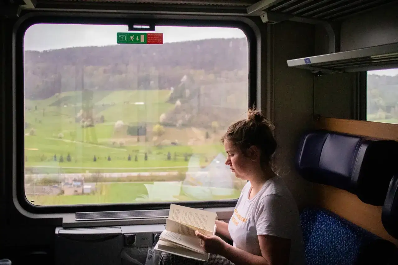 Junge Frau liest Buch im Zug, w&auml;hrend sie die gr&uuml;ne Landschaft auf ihrer Reise mit Interrail Italien genie&szlig;t.