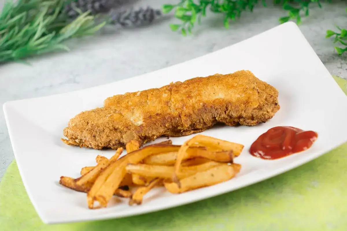 Knuspriges Fischfilet mit low carb panade, dazu Pommes und Ketchup auf einem weißen Teller.