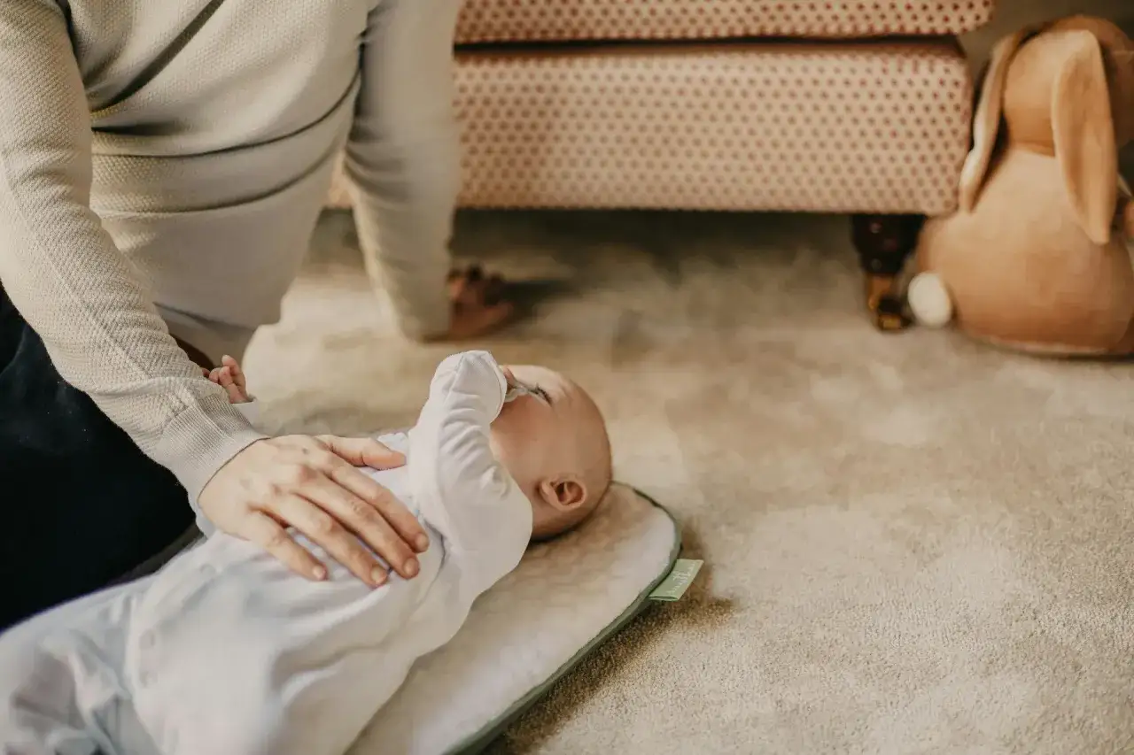 Ein Baby liegt auf einer Decke, die Hand einer Person streichelt es. Vielleicht sucht sie nach Hausmitteln gegen eine verstopfte Nase des Babys nachts.