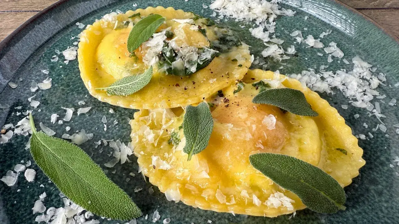 Zwei goldgelbe Mezzelune Spinaci, garniert mit frischem Salbei und Parmesan, auf einem dunkelgrünen Teller.