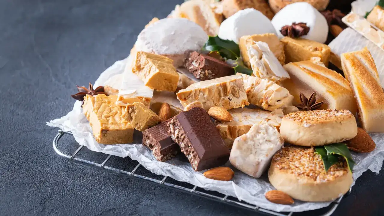 Variedad de postres navideños: turrones, polvorones, mazapanes y chocolates con almendras, listos para celebrar.