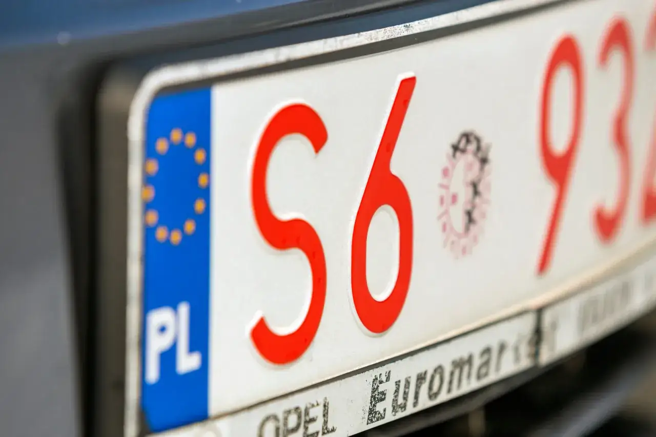 Zbliżenie na polskie tablice rejestracyjne z czerwonymi znakami. Widoczne litery