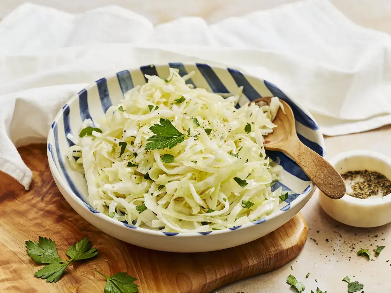 Frischer, selbstgemachter Krautsalat mit Petersilie und Pfeffer in einer gestreiften Sch&uuml;ssel, bereit zum Servieren.