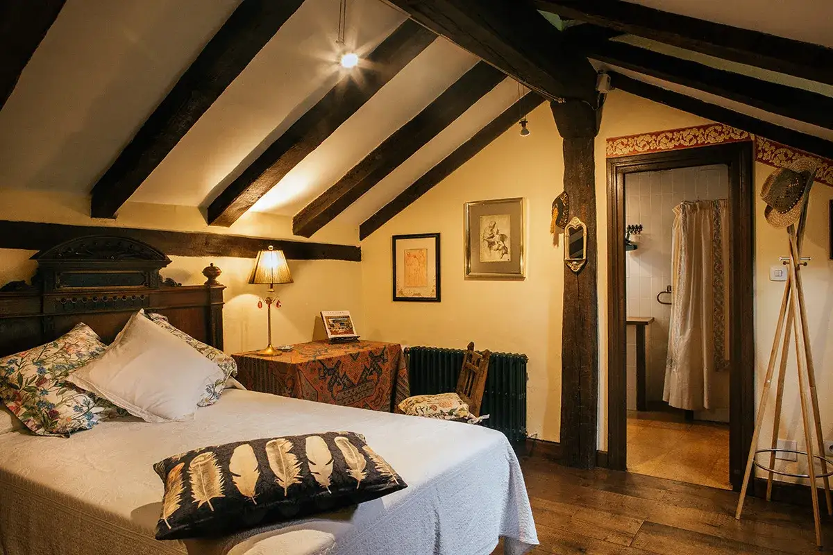 Acogedora habitación con vigas de madera, cama confortable y un rincón que evoca la tranquilidad de el molino de cabuérniga.