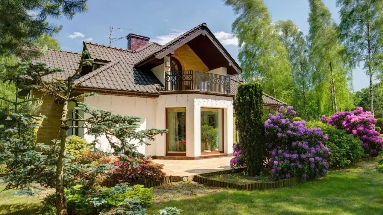 Piękny dom z wykuszem, otoczony kwitnącym ogrodem z rododendronami i iglakami.