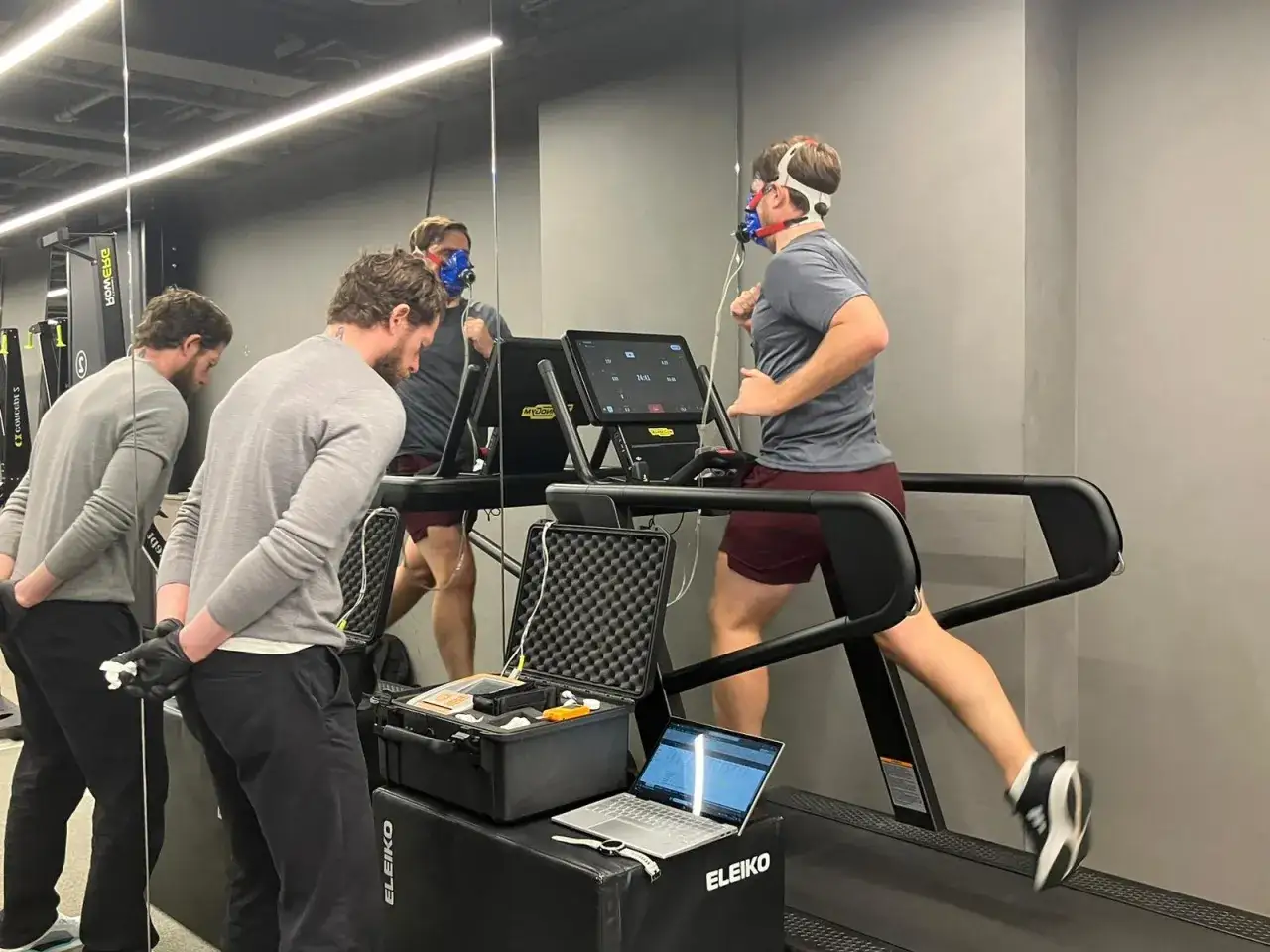 Man runs on treadmill with mask for VO2 max test, monitored by two men.
