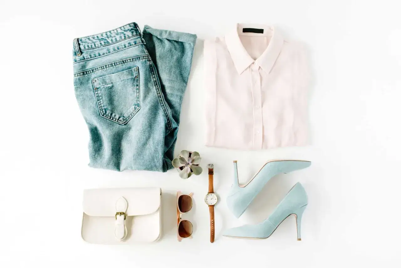 Ein minimalistischer Kleiderschrank: Jeans, hellrosa Bluse, weiße Tasche, Sonnenbrille, Uhr, Sukkulente und hellblaue Pumps.