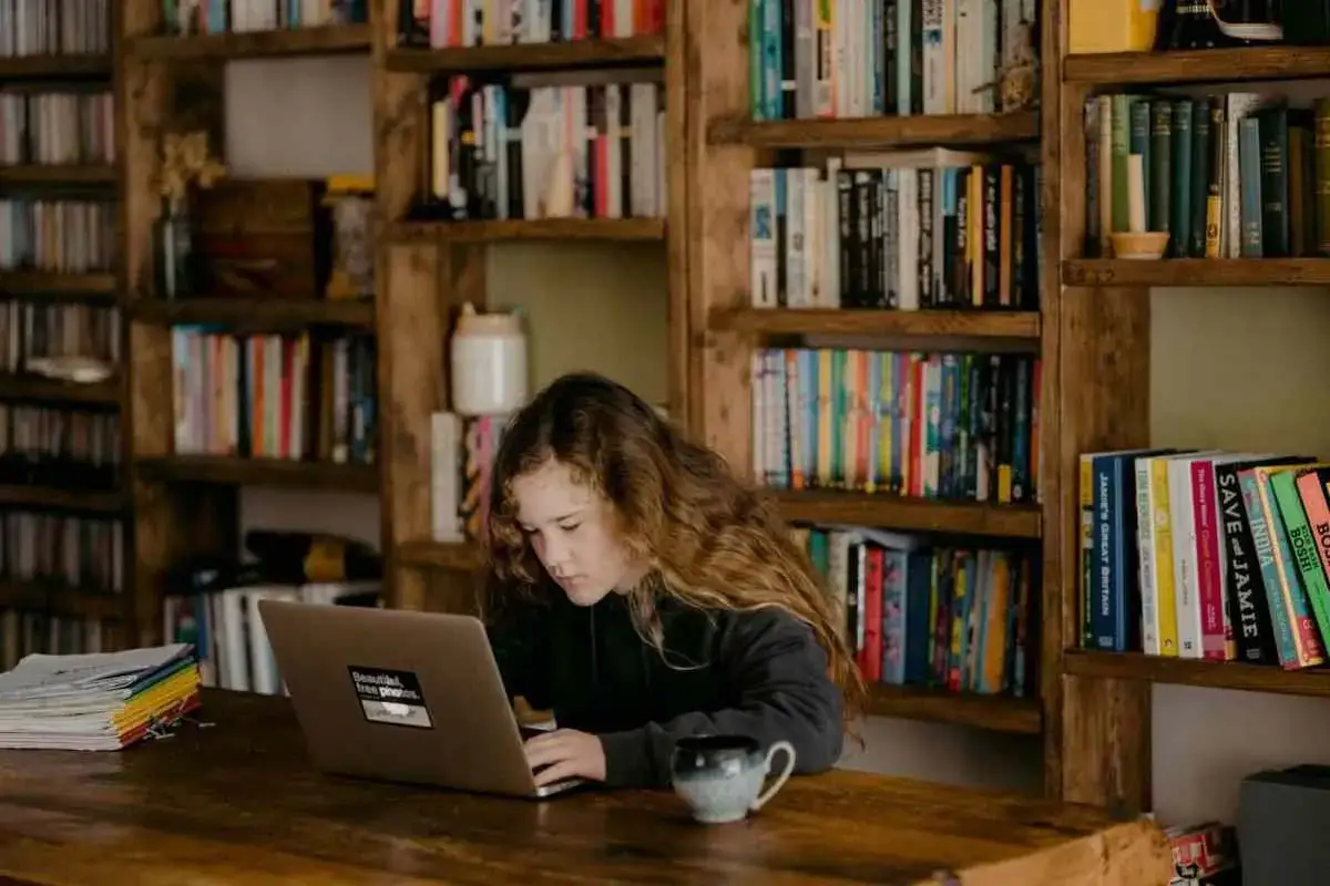 Dziewczynka z długimi włosami siedzi przy biurku, próbując skupić się na laptopie. Wokół niej piętrzą się książki, co może potęgować problemy z koncentracją.