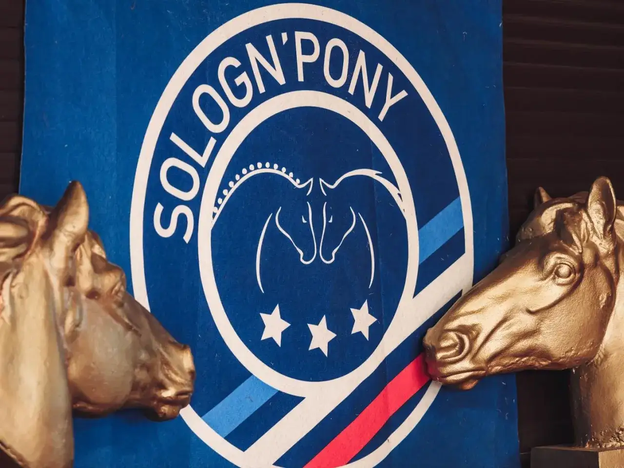 Deux têtes de chevaux dorées encadrent un logo 